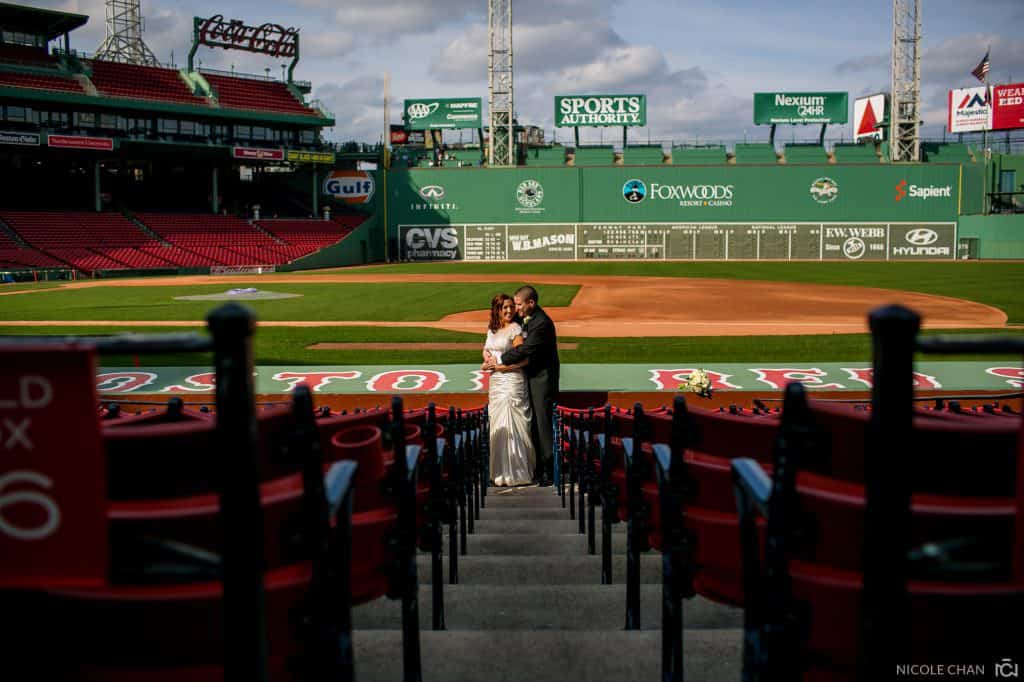 a bride and groom standing on the steps of a baseball field.