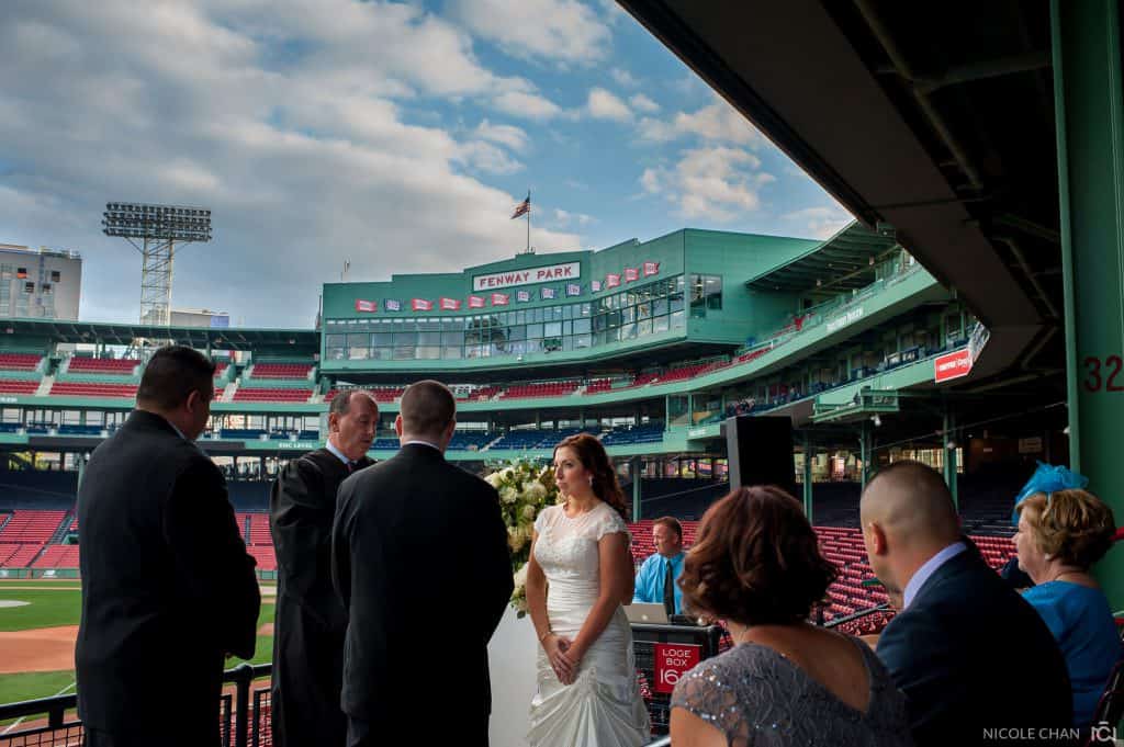a bride and groom standing at the end of a baseball field.