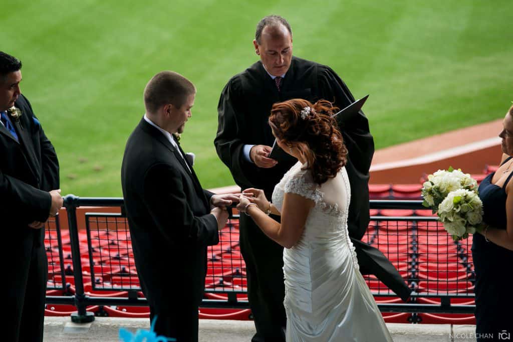 a bride and groom exchanging vows in front of a stadium.