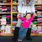 a woman and a little girl in front of a rack of shirts.
