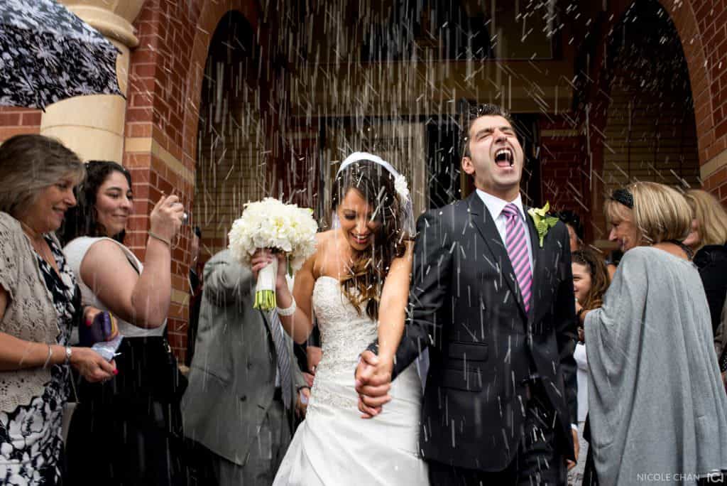 a bride and groom walking through the rain.
