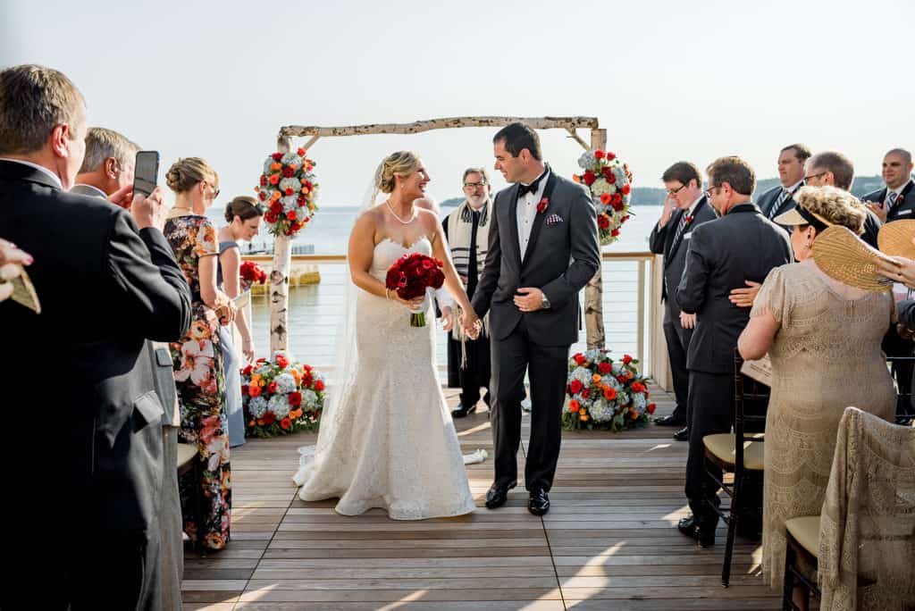 a bride and groom standing at the end of a dock.