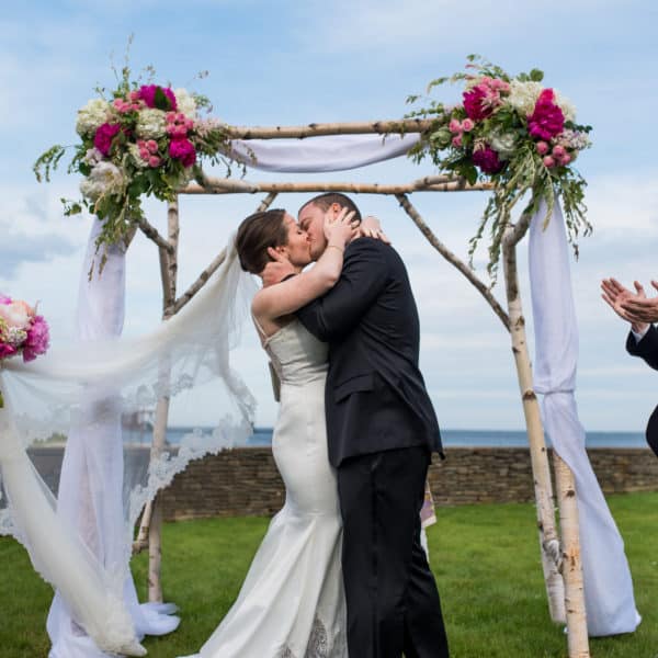 a bride and groom kissing under a wedding arch.