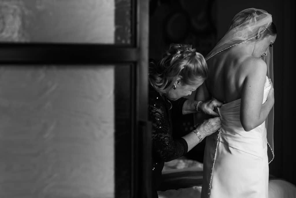 a woman helping another woman put on her wedding dress.