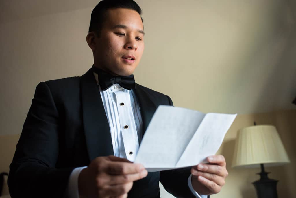 a man in a tuxedo reading a piece of paper.