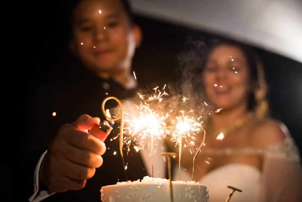 a bride and groom holding sparklers in front of a cake.