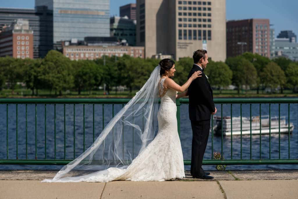 a bride and groom stand on a bridge overlooking the water.