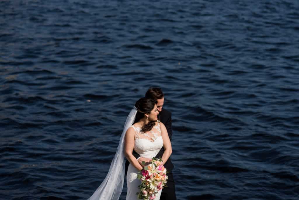 a bride and groom standing on a dock by the water.