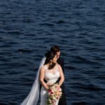 a bride and groom standing on a dock by the water.