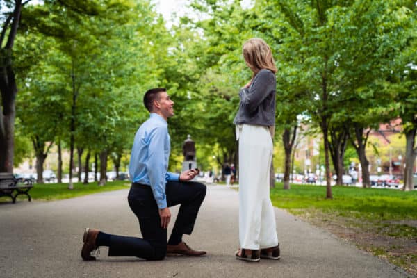 a man kneeling down next to a woman in a park.