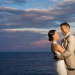 a bride and groom standing next to each other in front of a body of water.
