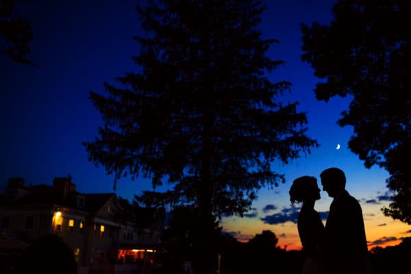 a bride and groom are silhouetted against the evening sky.