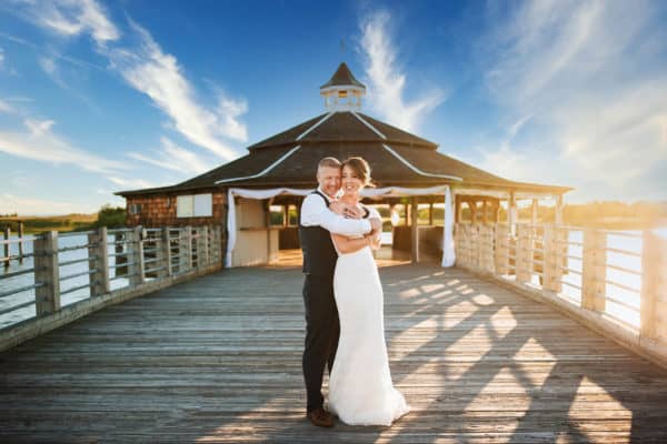 a bride and groom standing on a pier.