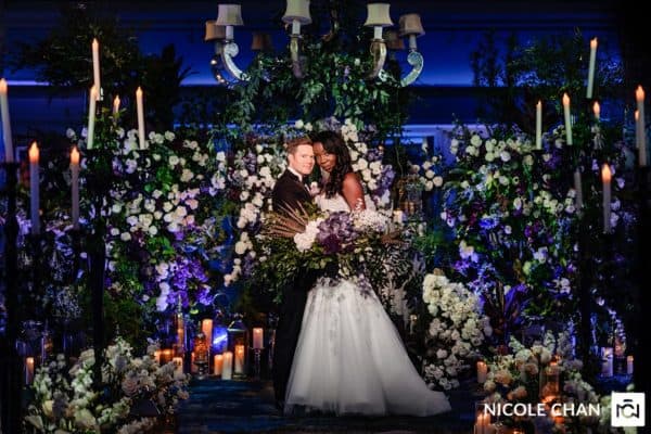 a bride and groom standing in front of a floral display.