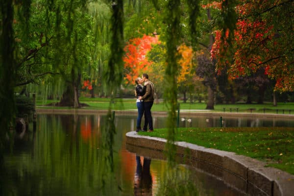 a man and a woman standing next to each other in front of a pond.