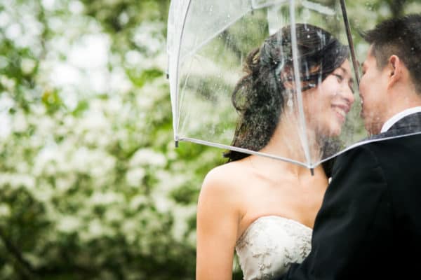 a bride and groom under an umbrella in the rain.