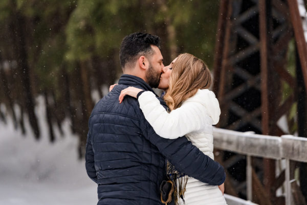 a man and a woman kissing on a bridge.