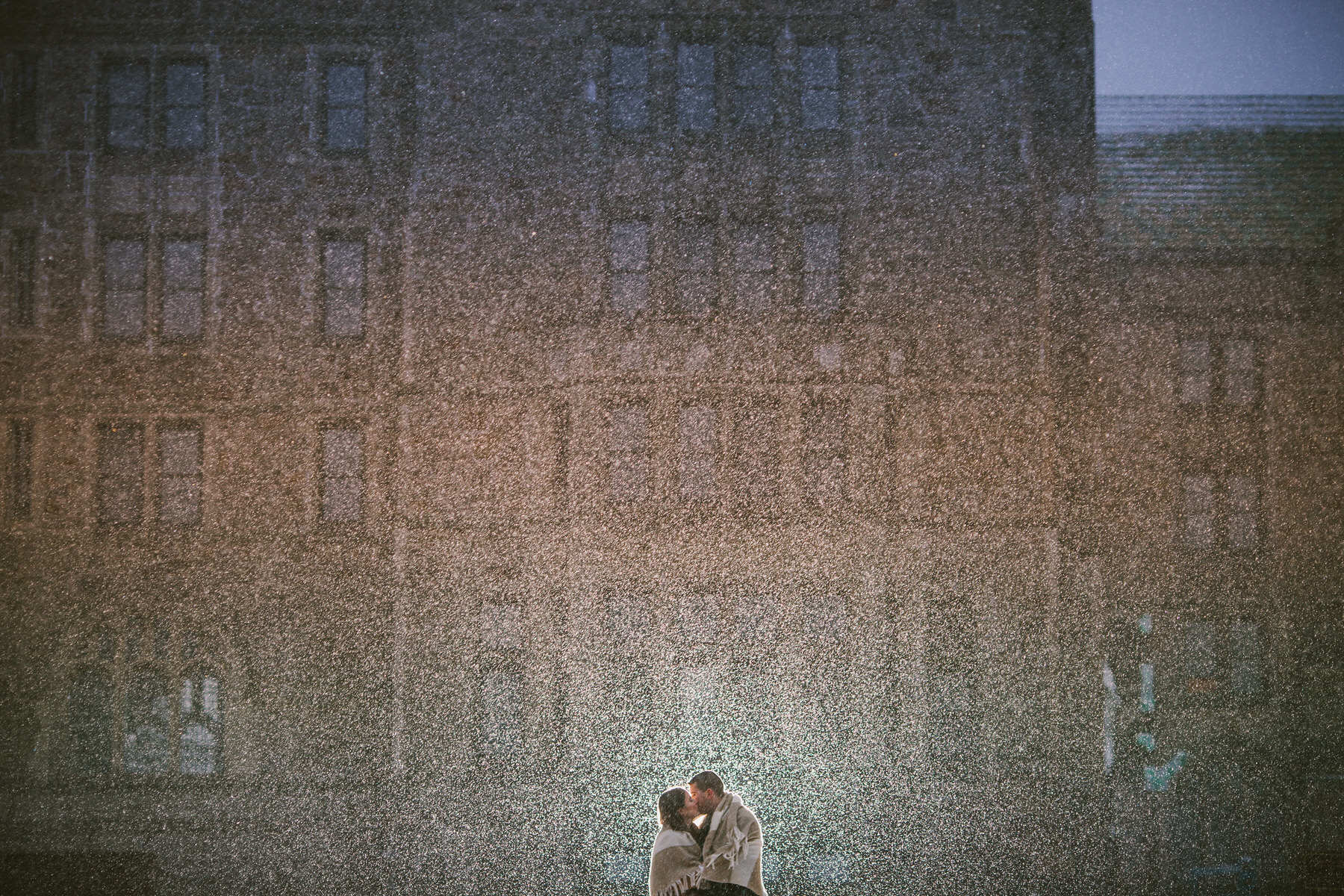 a couple kissing in front of a tall building.
