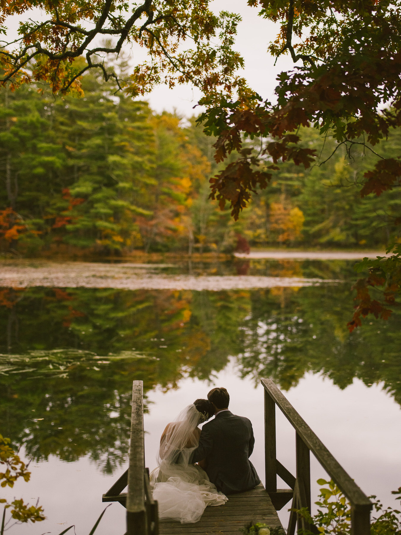 a bride and groom are sitting on a dock.