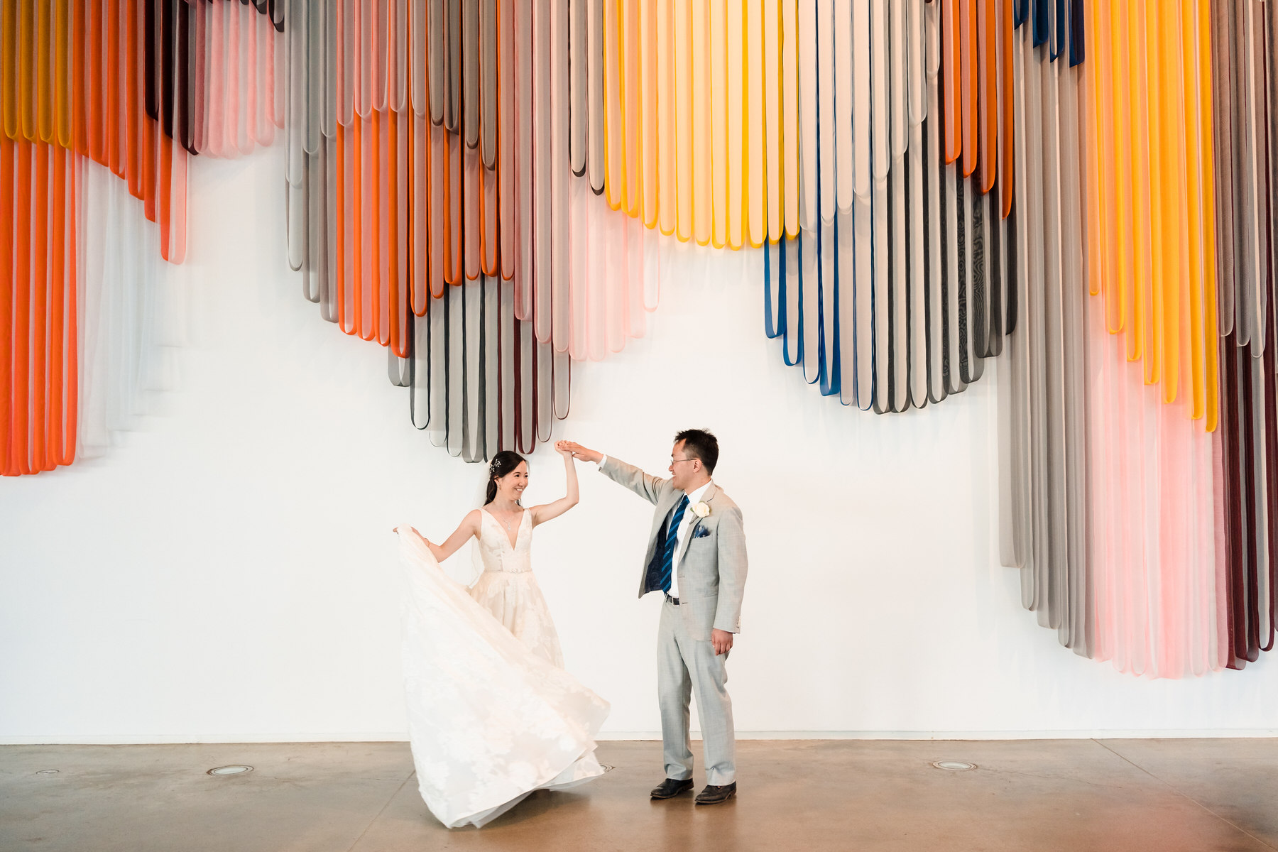 a bride and groom dancing in front of a colorful wall.