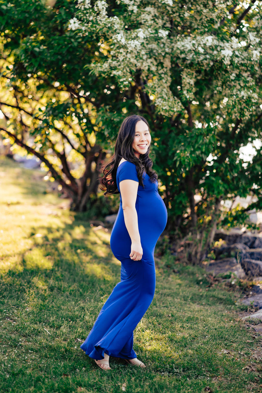 a pregnant woman in a blue dress standing in the grass.