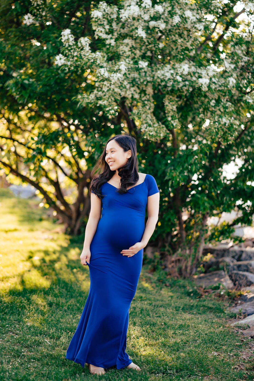 a pregnant woman in a blue dress standing in the grass.