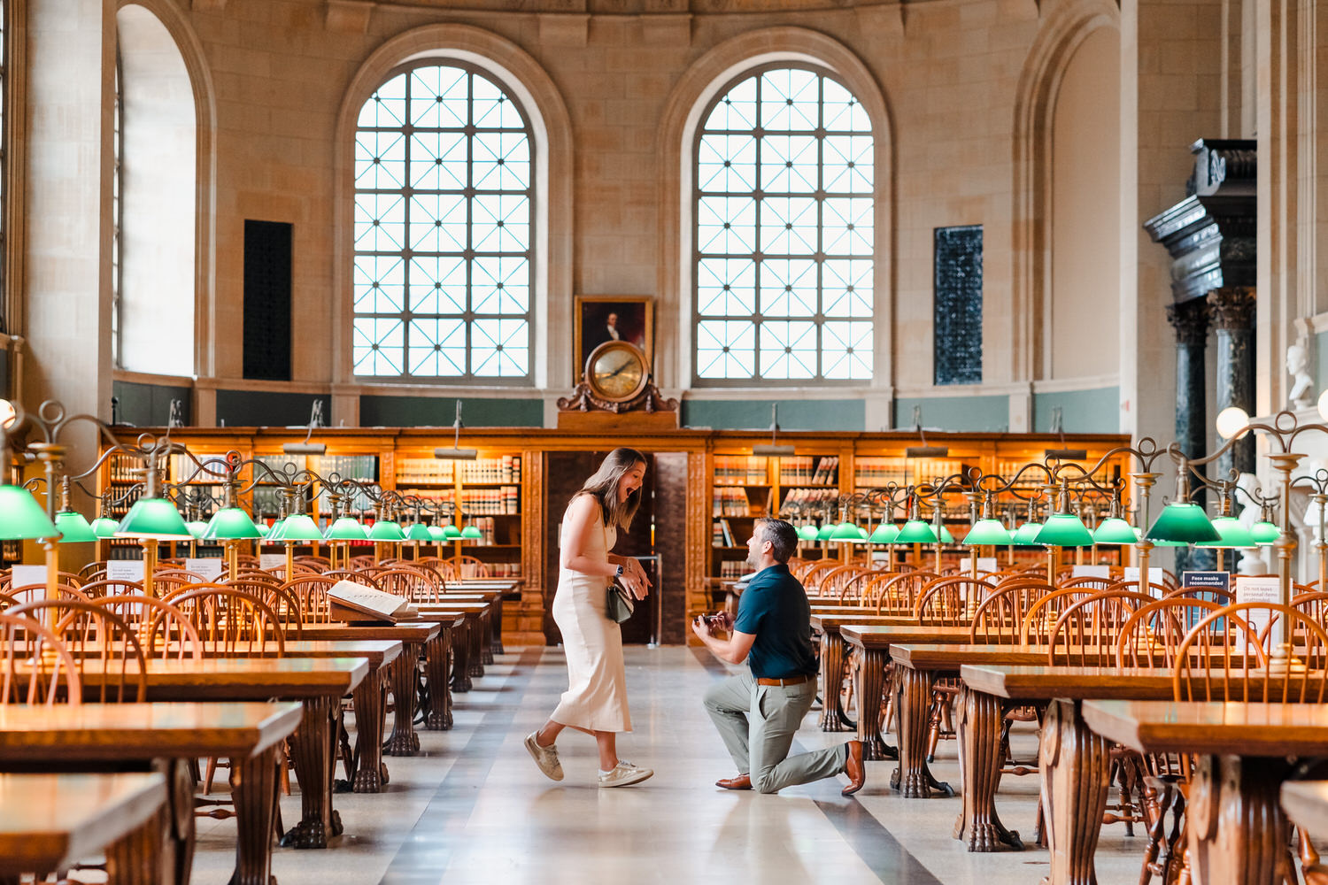 A Boston woman proposes while kneeling in front of a book in a library, captured by a proposal photographer.