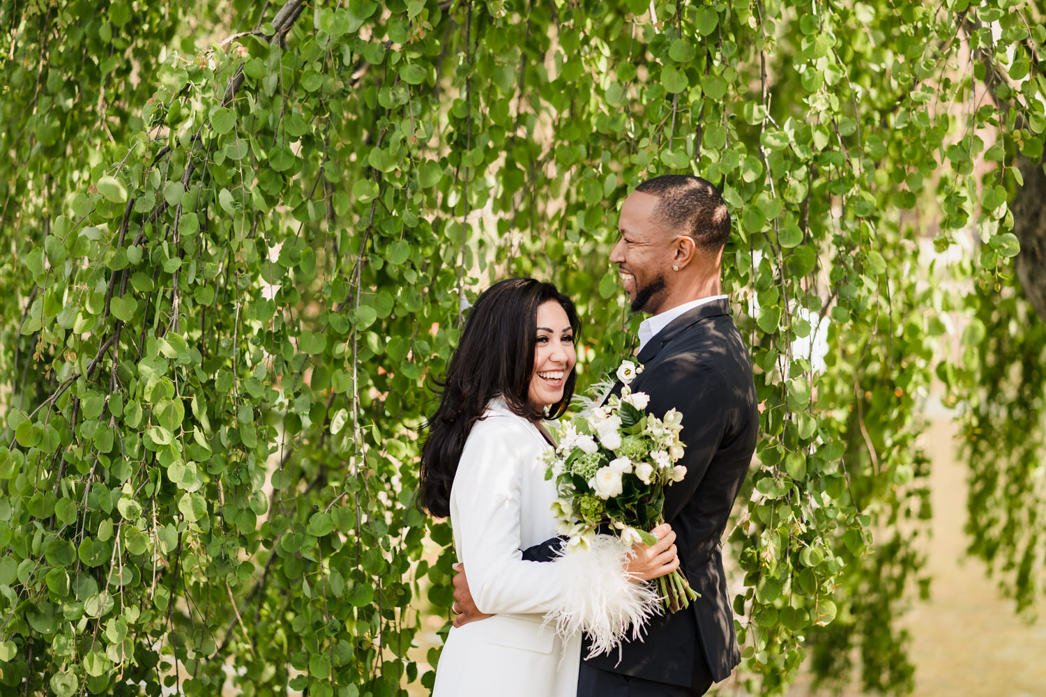 A bride and groom embracing under a willow tree during their Boston City Hall wedding.