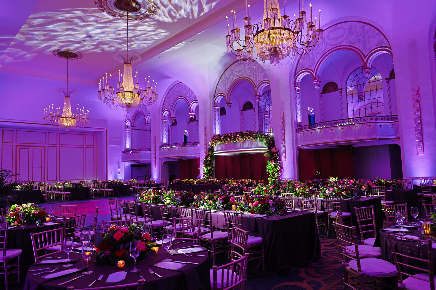 A large ballroom with purple lighting and tables.
