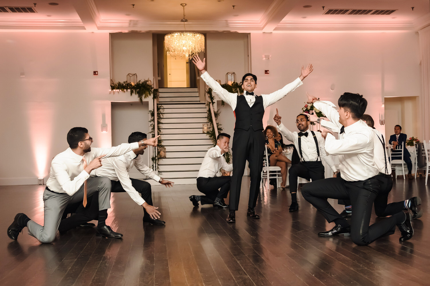 A man in a tuxedo dancing with a group of men in white shirts.